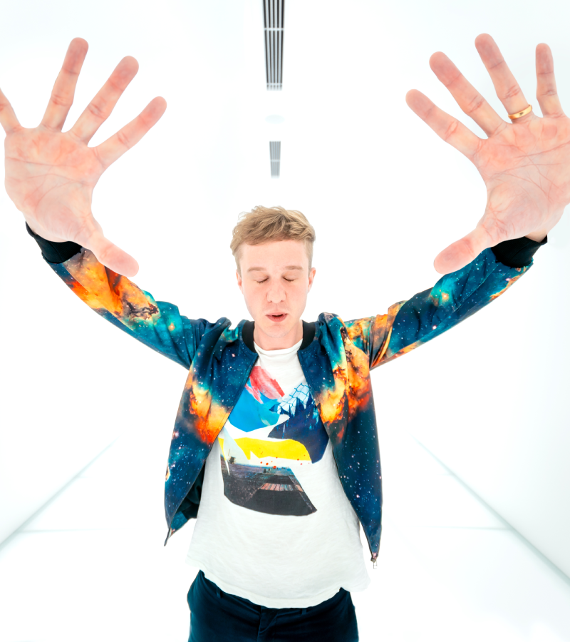 Ludvig Forssell in multicoloured top reaching arms out in stark white room