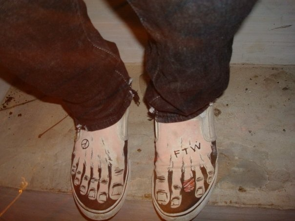 A photograph of someone's shoes, which are black fans with a semi-realistic bare feet design on them.
