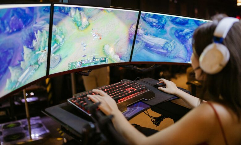 Three gaming monitors displaying cooperative multiplayer gameplay in a dark room