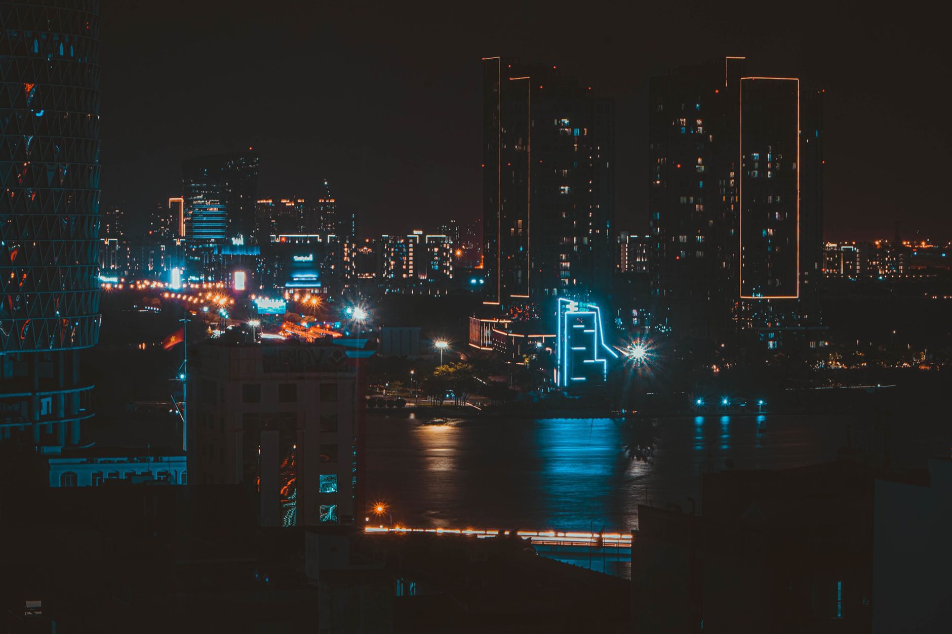 A neon-lit cityscape at night with reflective wet streets, evoking the visual style of Cyberpunk 2077s Night City
